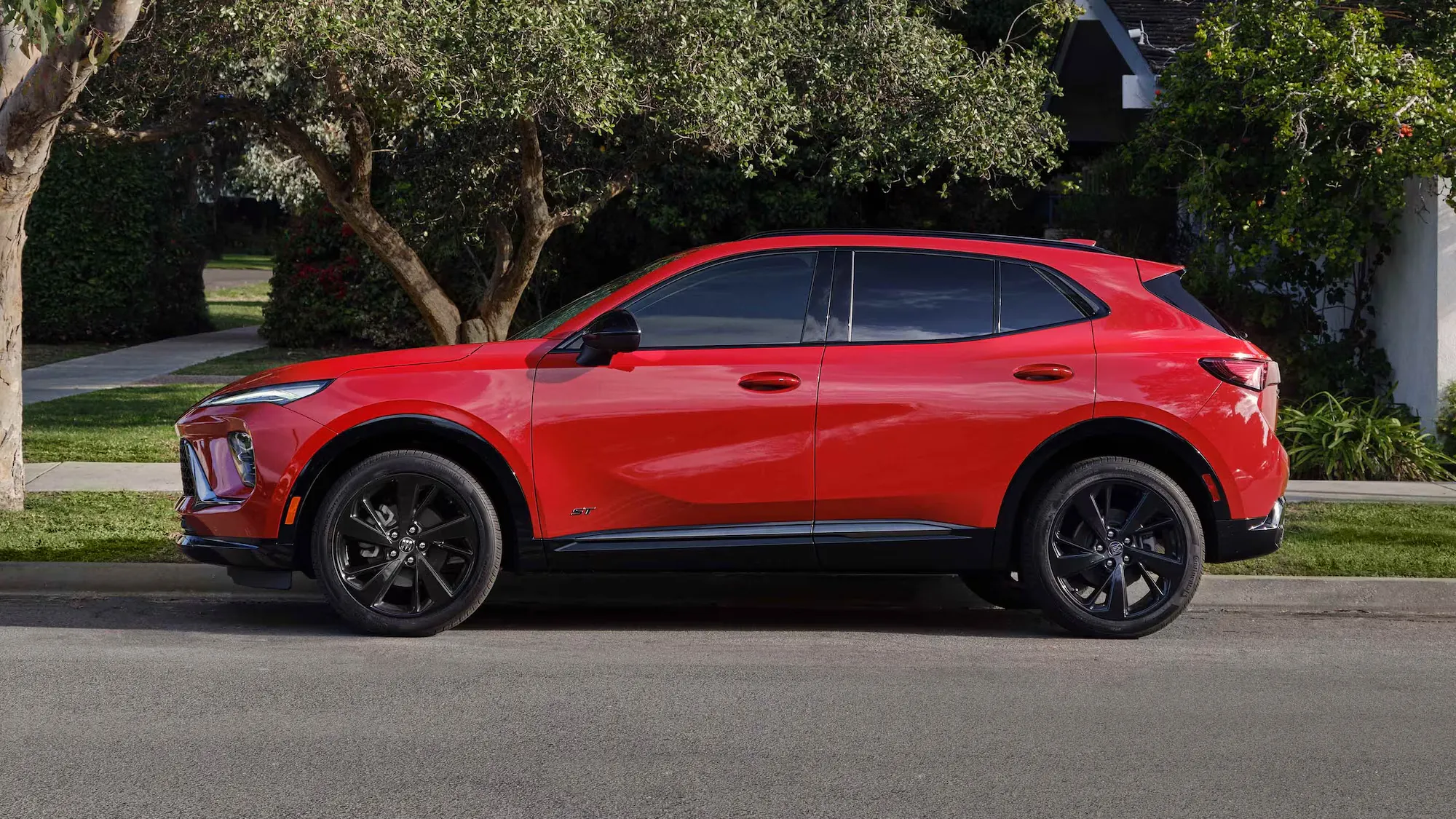 Buick Envision 2026 rouge vu de profil stationné devant une résidence.