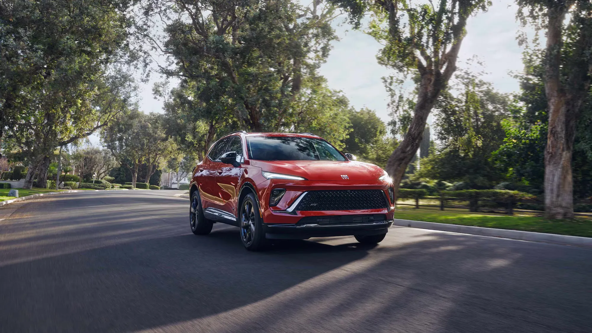 Buick Envision 2026 rouge roulant sur une rue bordée d’arbres.
