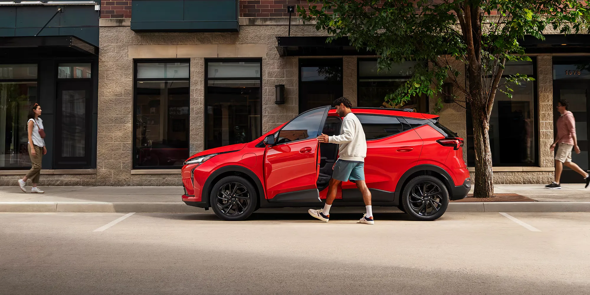 Chevrolet Bolt 2027 rouge stationné en bordure de rue devant des commerces.