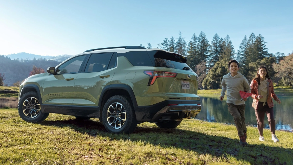 Chevrolet Equinox 2026 vert garé au bord de l'eau avec deux personnes à proximité. Un VUS compact 2026 pensé pour les sorties en famille.