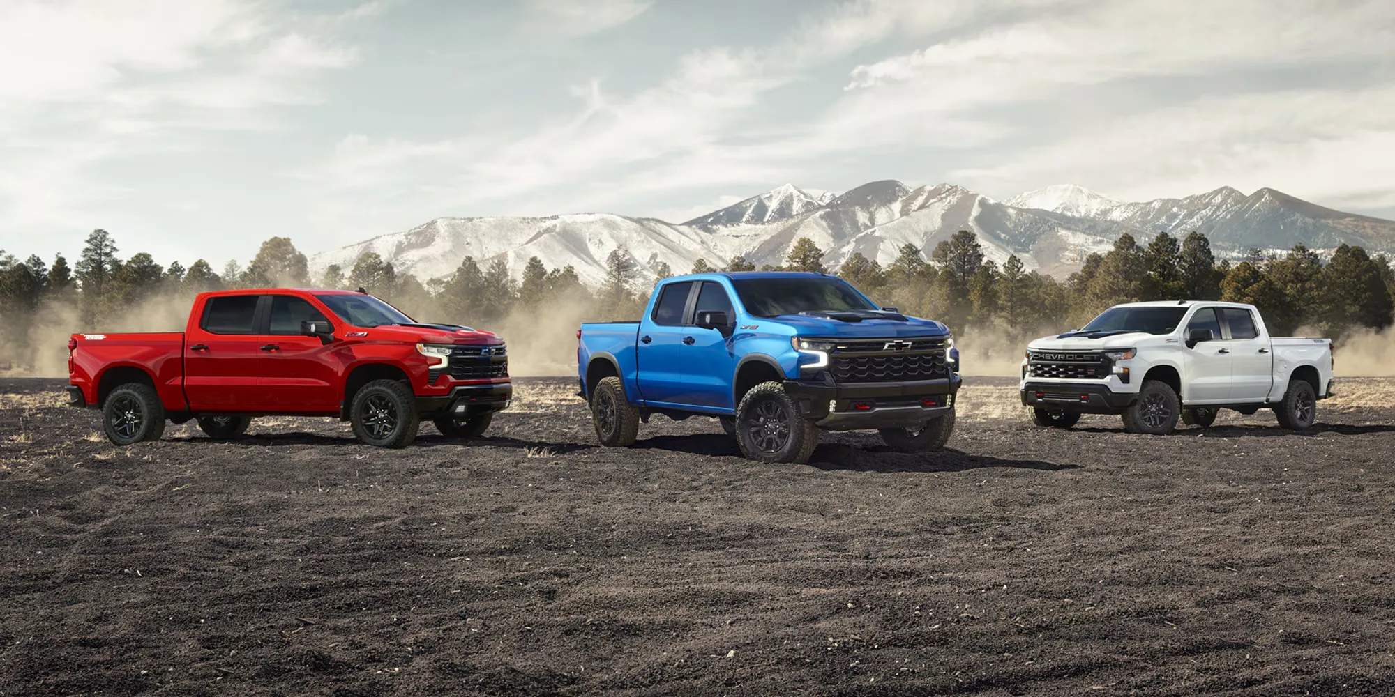 Trois Chevrolet Silverado 1500 2026 de couleurs différentes alignés devant un paysage de montagne.