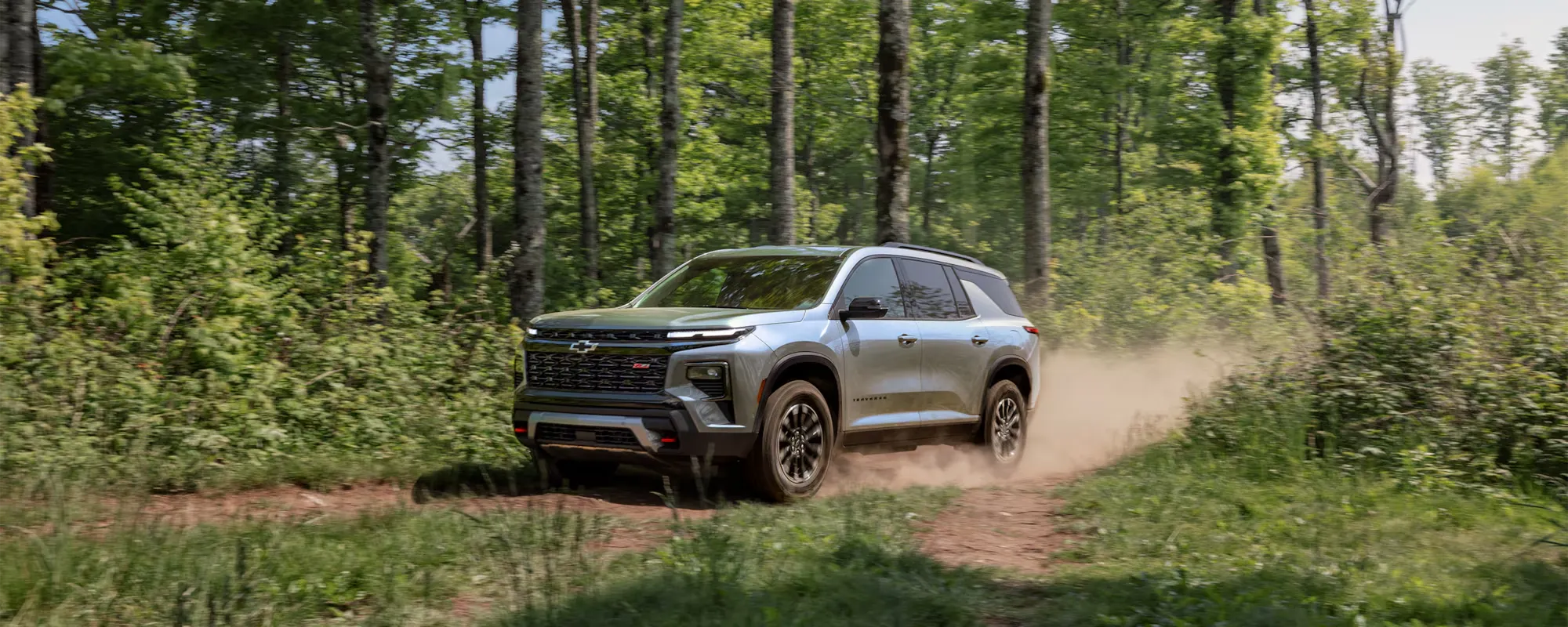 Chevrolet Traverse 2026 gris roulant sur un sentier forestier.