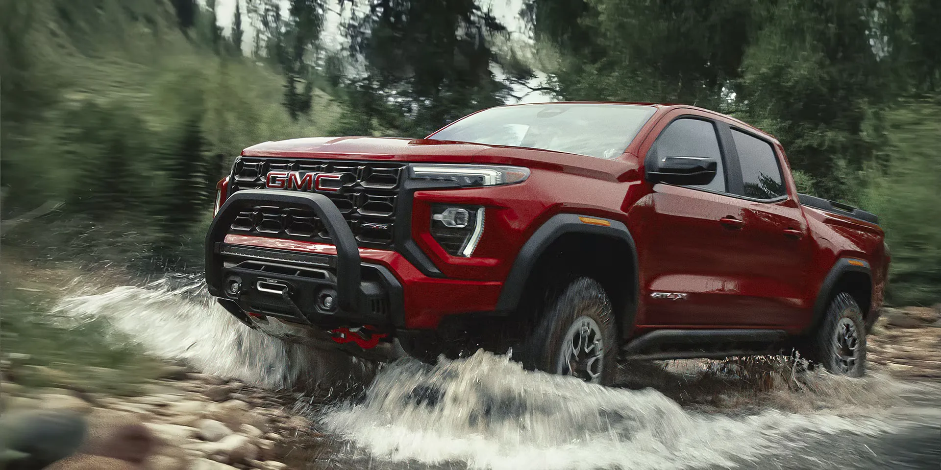 GMC Canyon 2026 rouge traversant un cours d’eau en conduite hors route.
