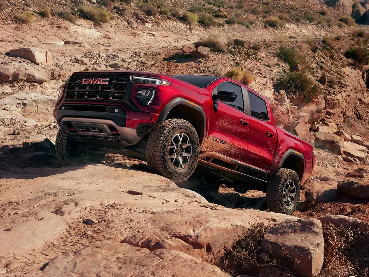 GMC Canyon 2026 rouge en montée sur un sentier rocheux.