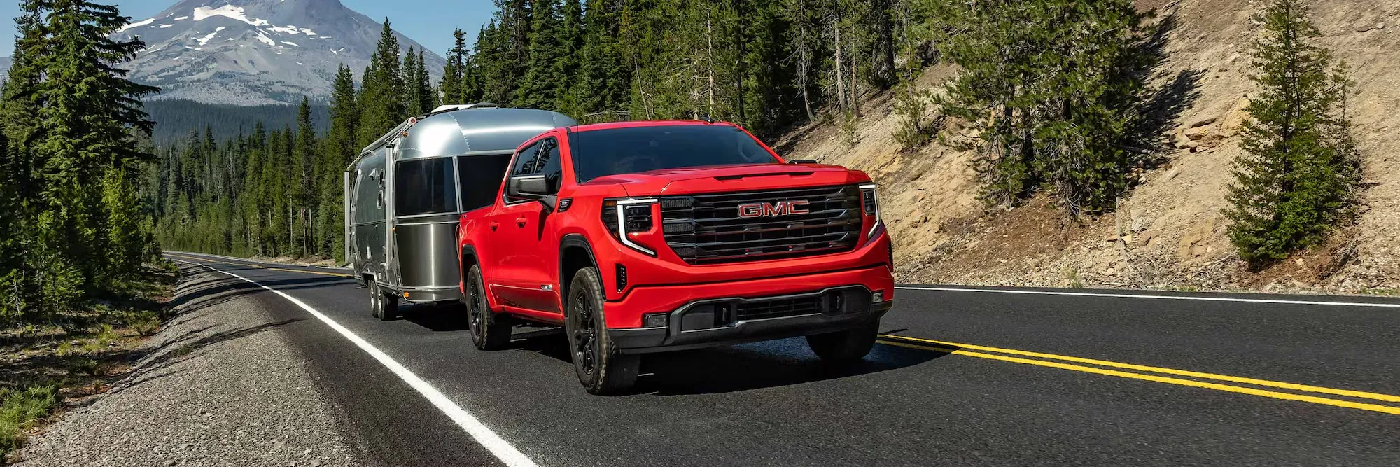 GMC Sierra 1500 2026 rouge remorquant une roulotte sur la route.
