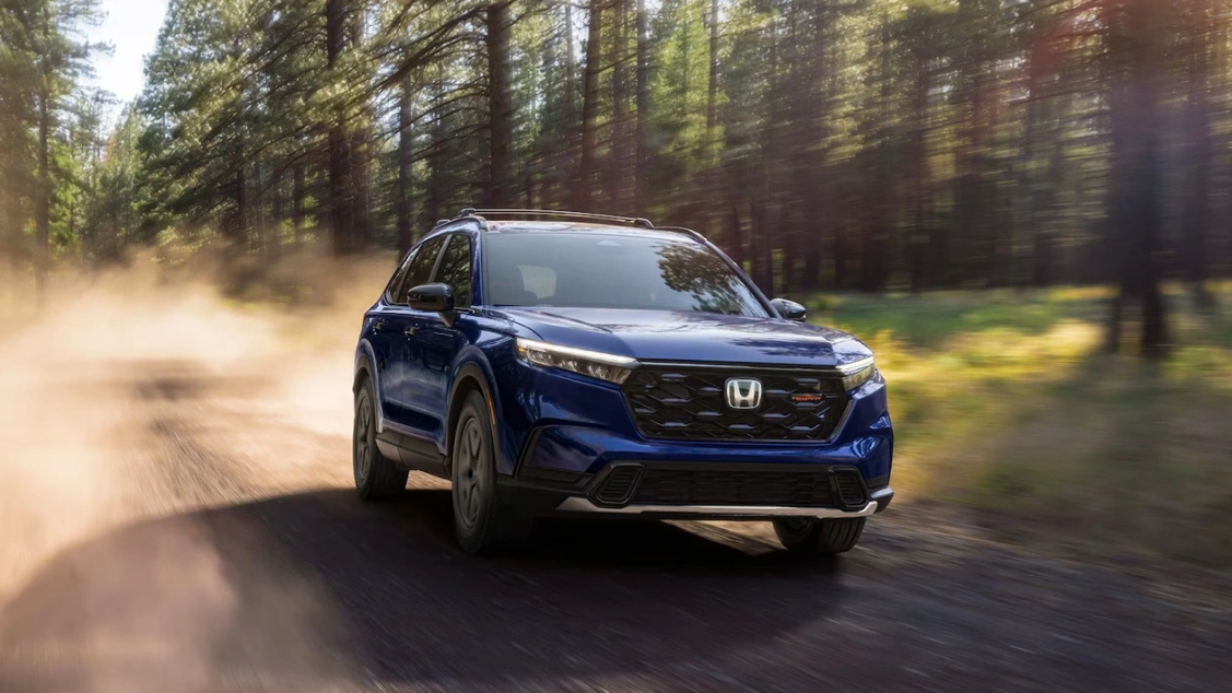 Honda CR-V 2026 bleu roulant sur un chemin bordé d'arbres. Un VUS compact 2026 reconnu pour sa capacité de chargement.