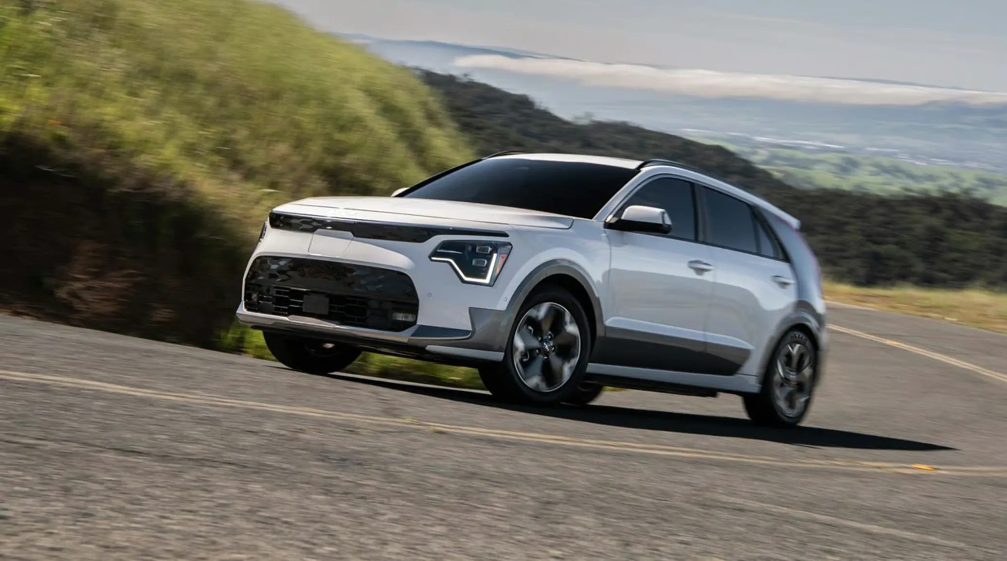 Kia Niro EV 2026 blanc en mouvement sur une route de campagne.