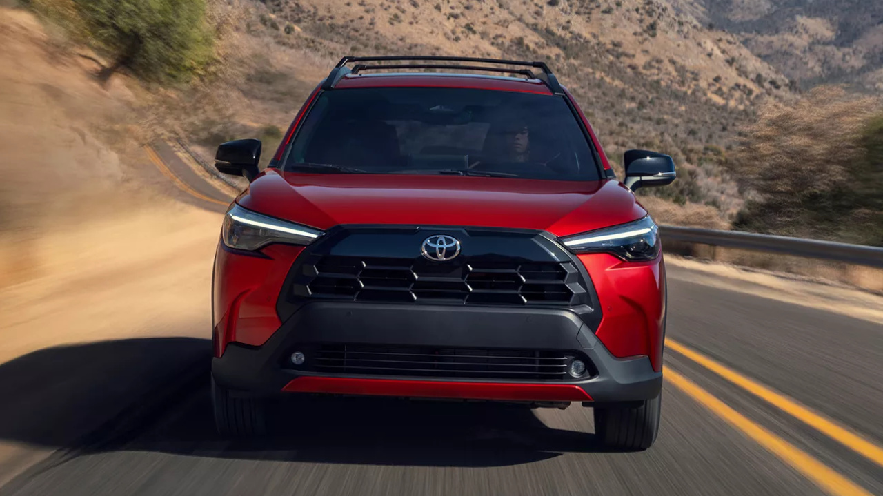 Toyota Corolla Cross 2026 rouge vu de face sur une route de montagne.