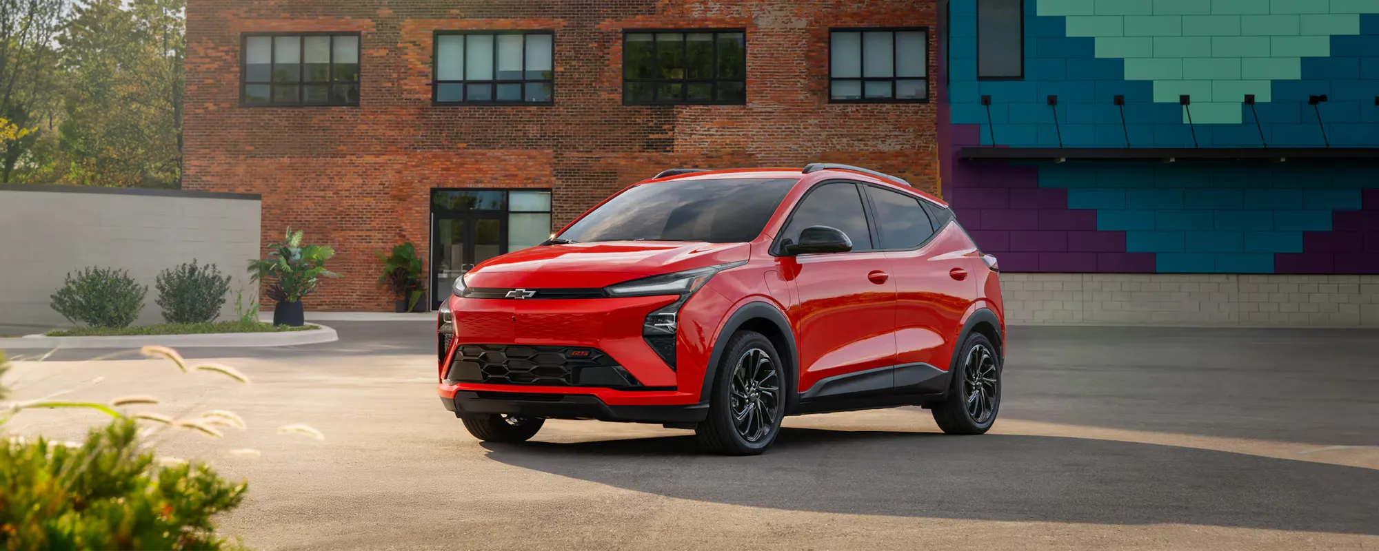 Chevrolet Bolt 2027 rouge stationné en ville pour aider à choisir entre Bolt et Nissan Leaf.