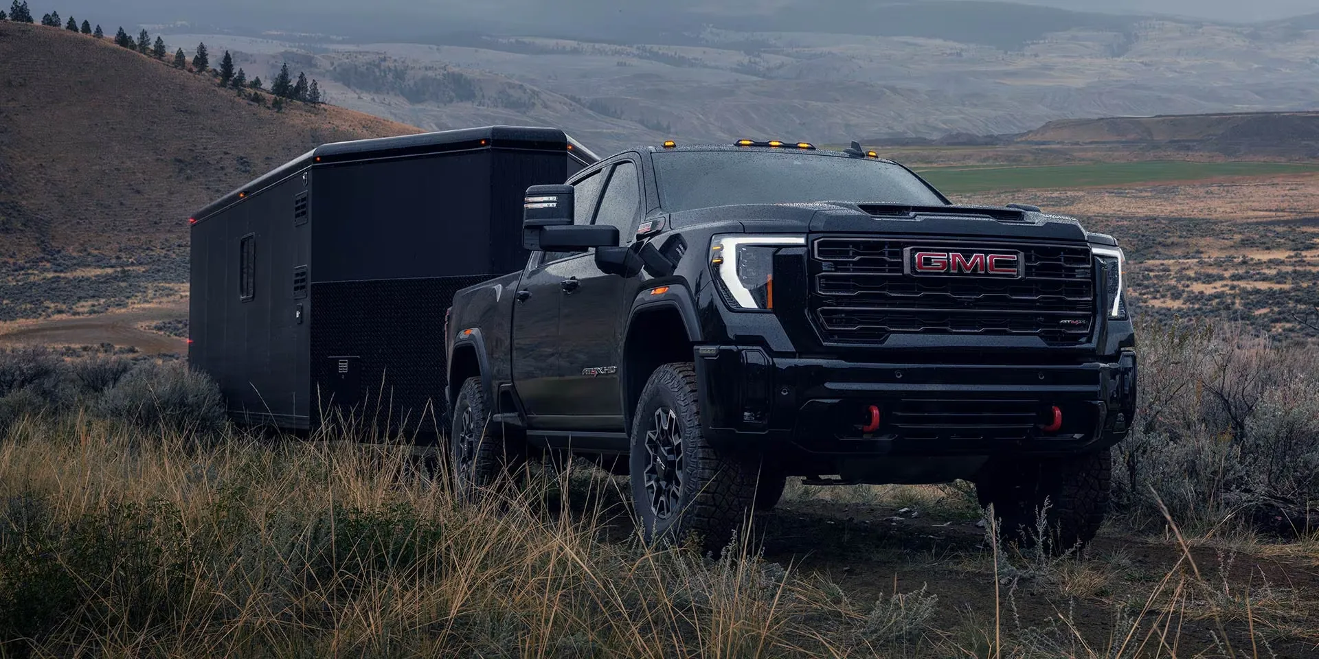 GMC Sierra 2500 HD 2026 noir remorquant une remorque fermée sur un terrain accidenté.