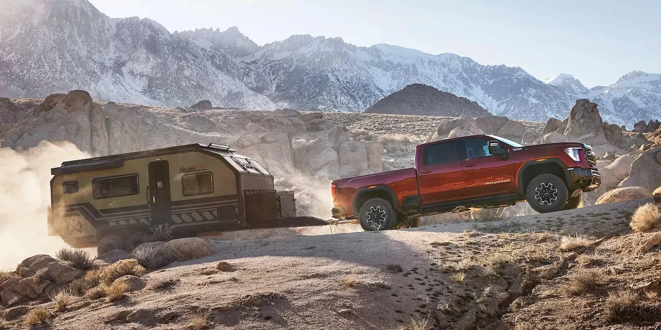 GMC Sierra 2500 HD 2026 remorquant une roulotte hors route devant des montagnes.